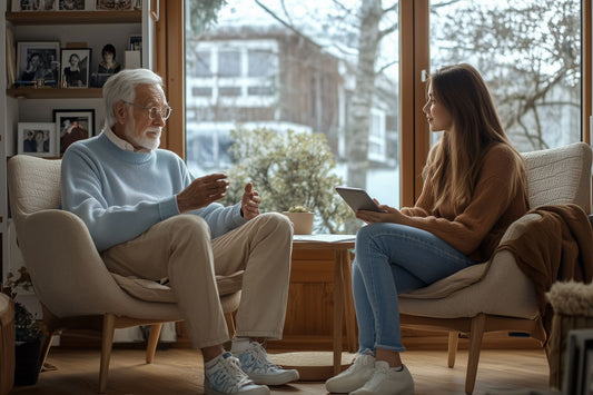 Un homme âgé partage ses souvenirs avec une jeune femme prenant des notes, dans un intérieur lumineux entouré de photos de famille.