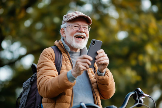 Un homme senior souriant, utilisant un smartphone en plein air, symbolisant l'accessibilité de la technologie pour partager des histoires.